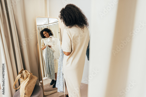Young stylish woman in fitting room looking at mirror trying on new clothes