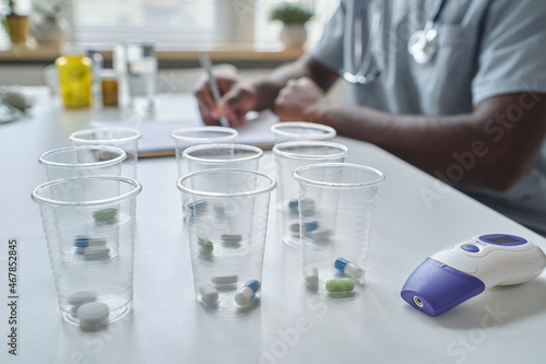 Close-up of glasses with pills inside of them standing on the table at hospital with doctor in the background