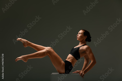 beautiful woman ballet dancer in black swimsuit posing on light grey studio background. Animal instinct