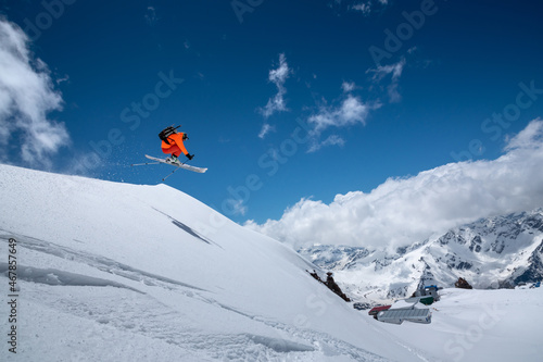 Flying in a jump over a slope Freestyle skier jumping in an orange ski suit in the snowy mountains on a sunny day
