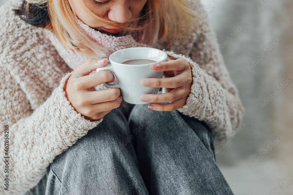 A girl with winter clothes enjoying a cup of hot chocolate on winter season at home A girl with winter clothes enjoying a cup of hot chocolate on winter season at home