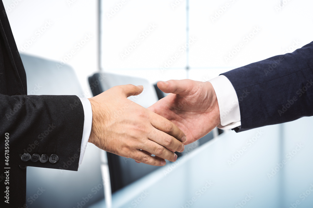Two businessmen shake hands on the background of sunny conference room, deal concept, close up