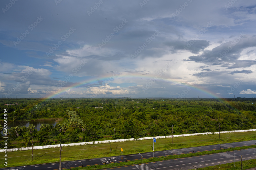 Rainbow over the lake and the forest on blue sky and white clouds background.Landscape rainbow in the country side.