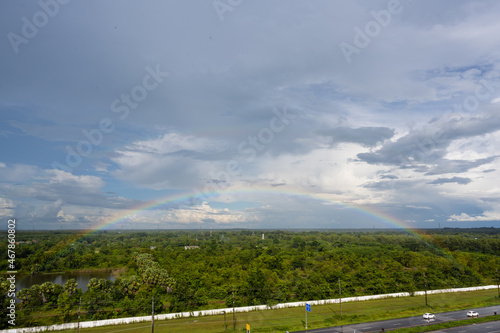 Rainbow over the lake and the forest on blue sky and white clouds background.Landscape rainbow in the country side.