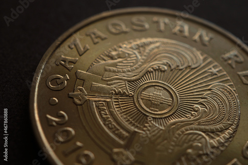 Translation: Kazakhstan. Kazakh 50 tenge coin with the country's emblem and focus on shanyrak. Dark brown tinted background or wallpaper about economy. Macro photo