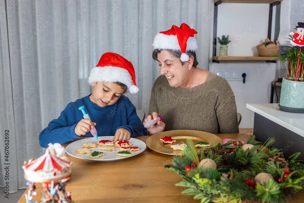 Little kid and his grandmother decorating christmas cookies at home