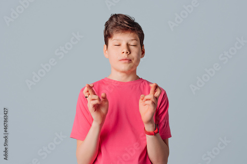 Hopeful handsome teenager boy cross fingers make wish, desperate superstitious guy make gesture hope believe in good luck, standing over gray background