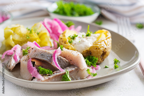 Herring with baked potato, onions and pickled cucumber on a plate. Traditional cuisine.