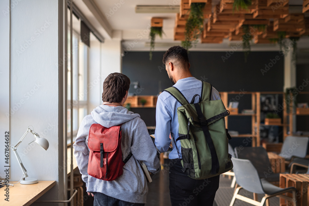 Rear view of young man with Down syndrome and his tutor indoors at school Rear view of young man with Down syndrome and his tutor indoors at school