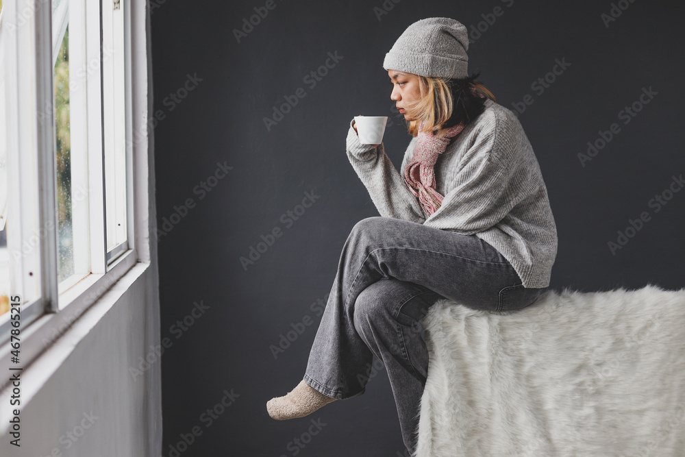 Lonely girl looking outside through the window on winter while enjoying a cup of coffee