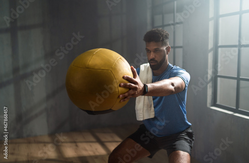 Young African American sportsman standing and lifting a medicine ball indoors, workout training