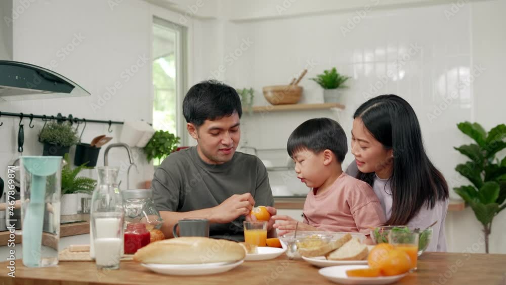 Asian family breakfast at home. Parents and children enjoy eating together, talking with laughter and good atmosphere. Father plays with son playfully at kitchen table. Asian family breakfast at home. Parents and children enjoy eating together, talking with laughter and good atmosphere. Father plays with son playfully at kitchen table.