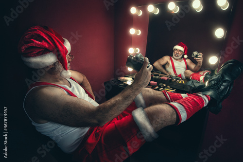 Narcissistic Santa Claus looking at the mirror and making selfie with vintage camera