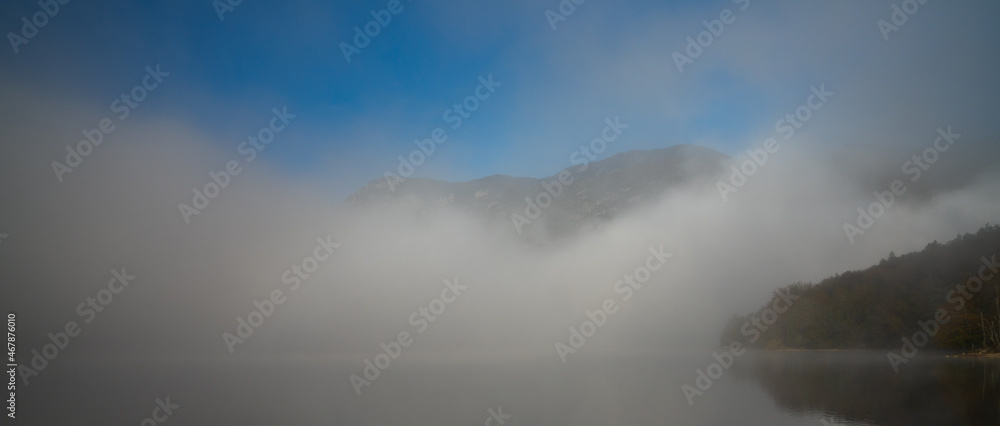 panorama horizontal landscape of a calm lake with thick fog and forest in the mist under a blue sky