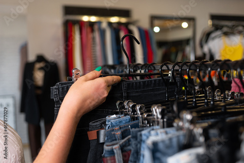 female hand sorting through hangers with jeans in a store, women's clothing on racks, a choice of trousers in a boutique.