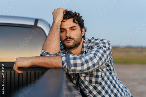 Young white man looking at camera while leaning on car trunk