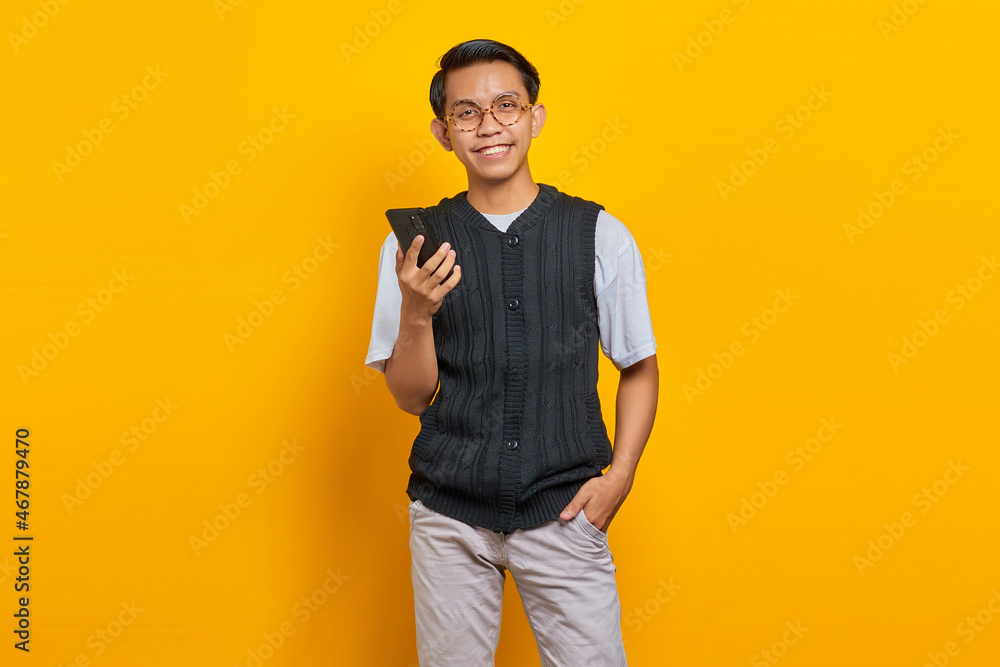 Smiling young Asian man talking on mobile phone and looking at camera over yellow background Smiling young Asian man talking on mobile phone and looking at camera over yellow background