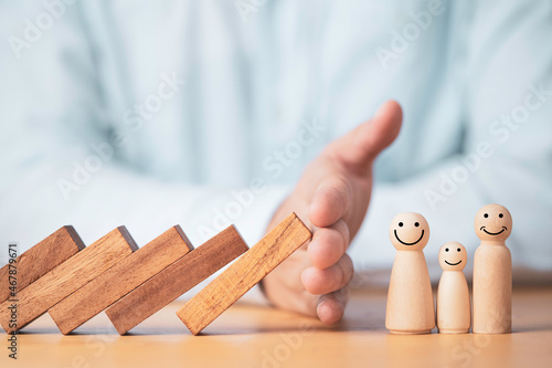 Businessman hand gesture protecting wooden domino falling to family dolls for insurance and assurance concept. photo