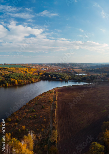 Aerial vertcal view of lake at sunrise in autumn. Meadows, trees at dawn. Colorful aerial landscape of river coast at sunset in fall. Plowed fields, harvested crops, dry corn. Horodok Ukraine