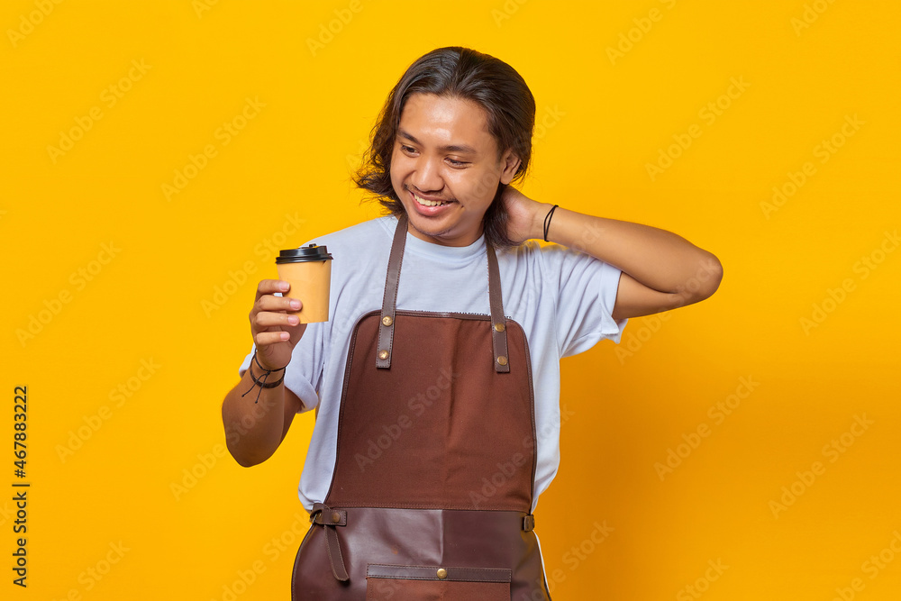 Portrait of handsome man wearing apron looking at cup of coffee being held isolated on yellow background Portrait of handsome man wearing apron looking at cup of coffee being held isolated on yellow background