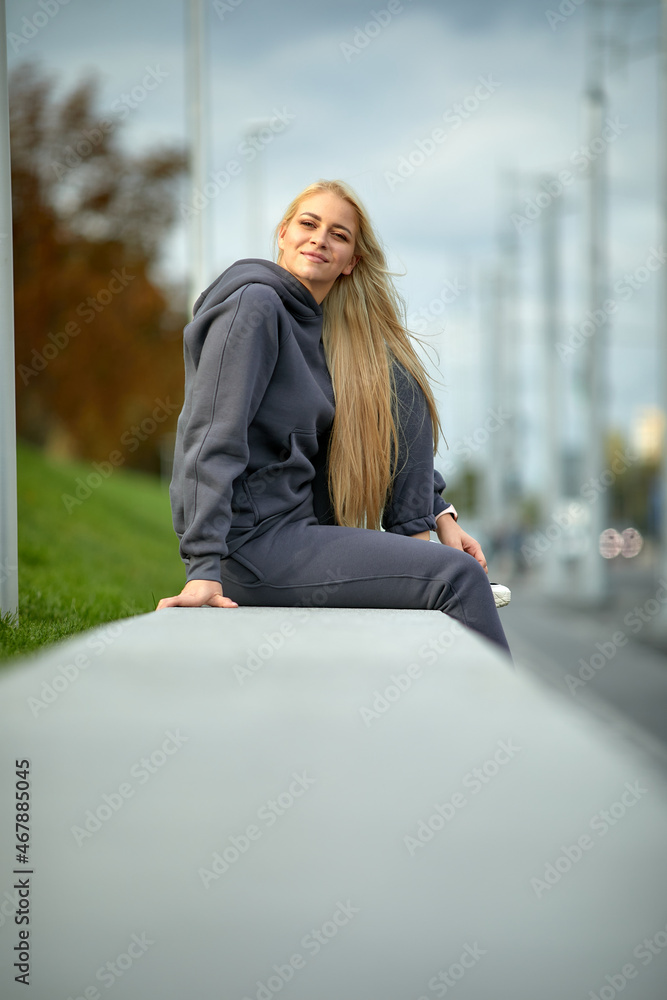 Fototapeta premium A young girl in a tracksuit stands in a city park