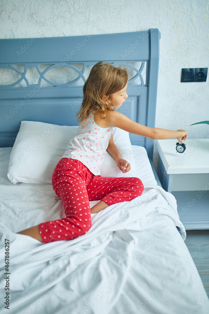 Little girl turns on an alarm clock, wakes up from sleep on a big and cozy bed Little girl turns on an alarm clock, wakes up from sleep on a big and cozy bed