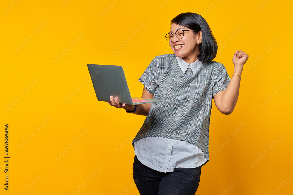 Portrait of excited Asian woman holding laptop over yellow background Portrait of excited Asian woman holding laptop over yellow background