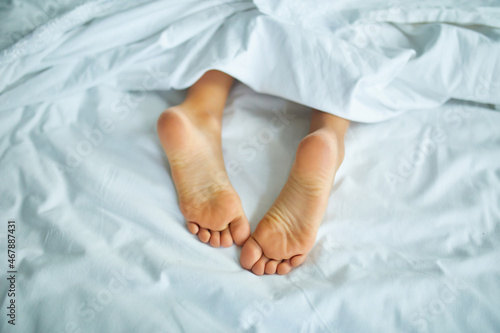 Girl's feet covered with white bed sheet, sleeping in a comfortable bed