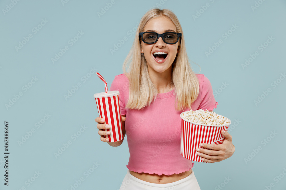 Young smiling cheerful woman 20s in 3d glasses watch movie film hold bucket of popcorn cup of soda pop isolated on plain blue background studio portrait. People emotions in cinema lifestyle concept.
