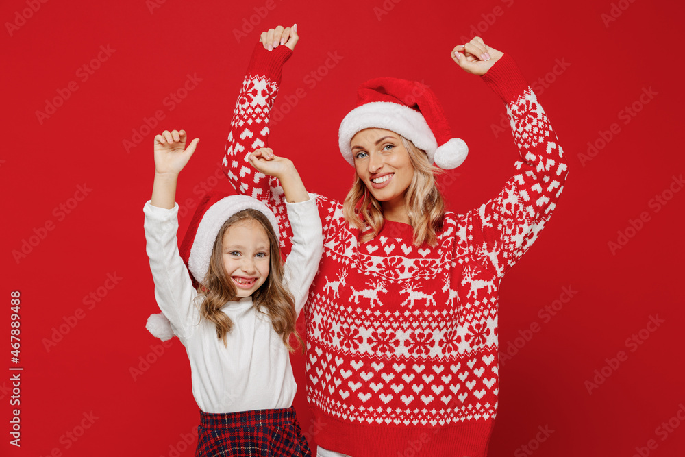 Young smiling woman in sweater hat have fun with child baby girl 6-7 years old. Mommy little kid daughter dancing rejoicing isolated on plain red color background studio. New Year love family concept. Young smiling woman in sweater hat have fun with child baby girl 6-7 years old. Mommy little kid daughter dancing rejoicing isolated on plain red color background studio. New Year love family concept.