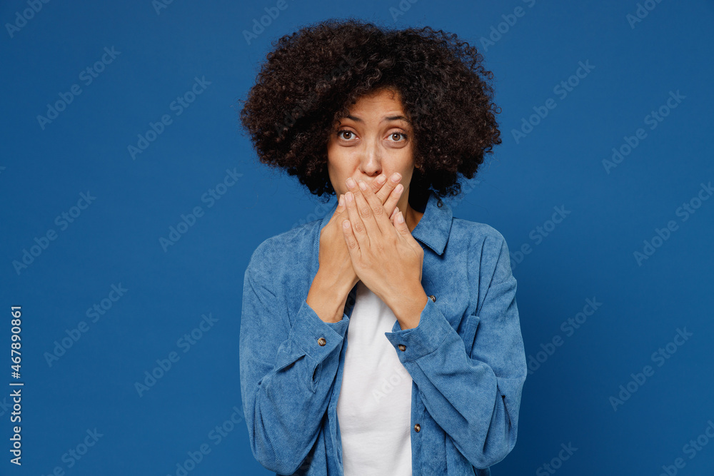 Young shocked astonished impressed upset black woman 20s in casual clothes shirt white t-shirt cover mouth with hand isolated on plain dark blue background studio portrait. People lifestyle concept. Young shocked astonished impressed upset black woman 20s in casual clothes shirt white t-shirt cover mouth with hand isolated on plain dark blue background studio portrait. People lifestyle concept.