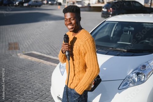 African American man charging his electric car. © Serhii