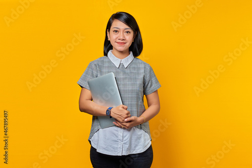 Portrait of beautiful smiling woman holding laptop isolated on yelllow background