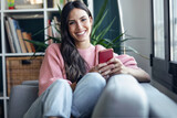 Pretty smiling woman using mobile phone sitting on a couch at home