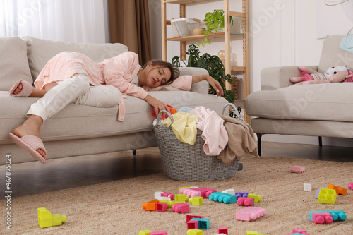Tired young mother sleeping on sofa in messy living room photo