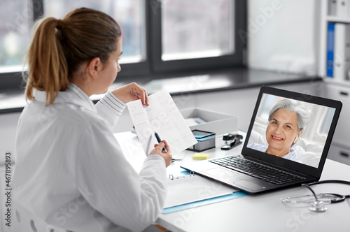 healthcare  technology and medicine concept - female doctor in white coat with laptop computer and cardiogram having video call with patient at hospital
