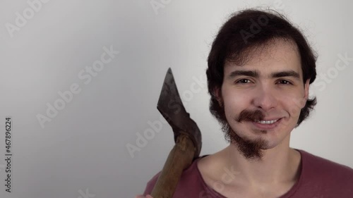 Portrait of smiling man showing that behind the axe which he holds he has not shaven all beard. Funny guy with trimmed part of his face. Person has one smooth cheek and a piece of mustache on another.