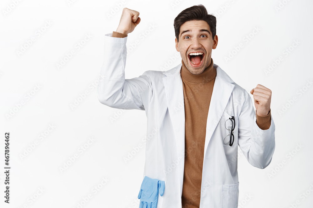 Enthusiastic medical worker, doctor in robe cheering, shouting from joy, winning, standing over white background Enthusiastic medical worker, doctor in robe cheering, shouting from joy, winning, standing over white background