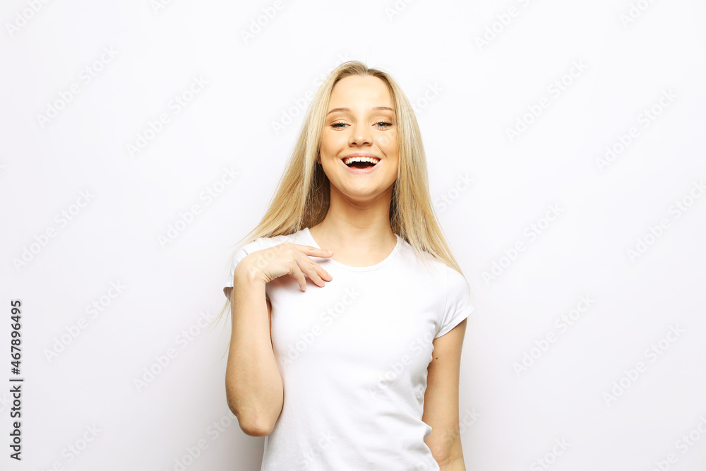 Young cute smiling blond woman wearing white t-shirt over light grey background. Young cute smiling blond woman wearing white t-shirt over light grey background.