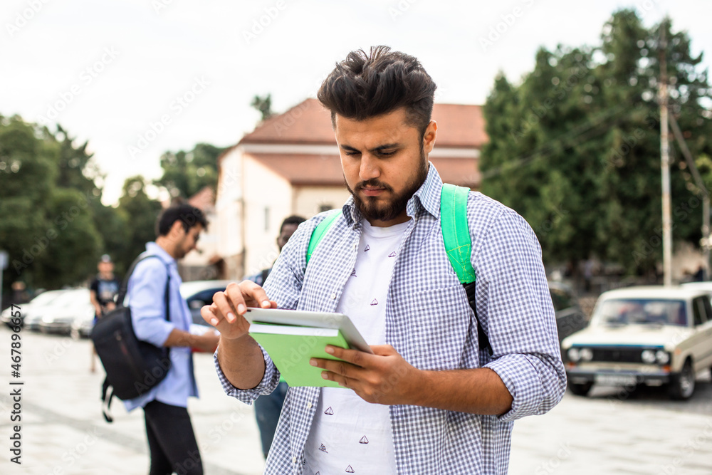The indian student stands outdoors and holds a stack of books The indian student stands outdoors and holds a stack of books