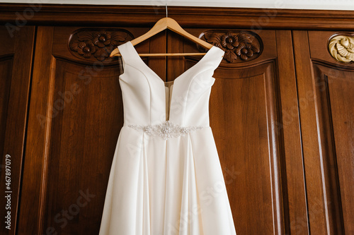 Fashionable beautiful classic lace silk wedding dress hanging on hanger in hotel wooden room. morning preparation wedding concept.
