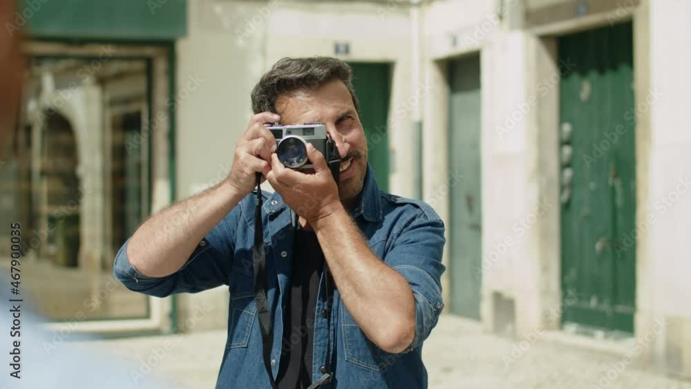 Front view of happy man taking picture of his lover in street. Slider shot of bearded Caucasian male person holding camera, smiling, taking photo during trip on summer day. LGBT, photoshoot concept Front view of happy man taking picture of his lover in street. Slider shot of bearded Caucasian male person holding camera, smiling, taking photo during trip on summer day. LGBT, photoshoot concept