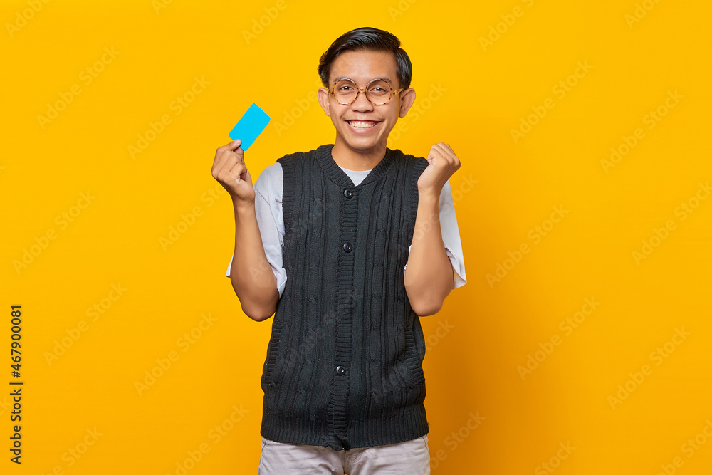Excited young Asian man holding credit card isolated on yellow background Excited young Asian man holding credit card isolated on yellow background