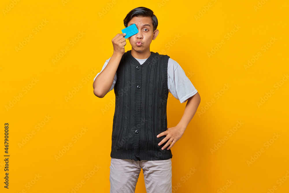 Smiling young handsome man covering eye with a credit card on yellow background Smiling young handsome man covering eye with a credit card on yellow background