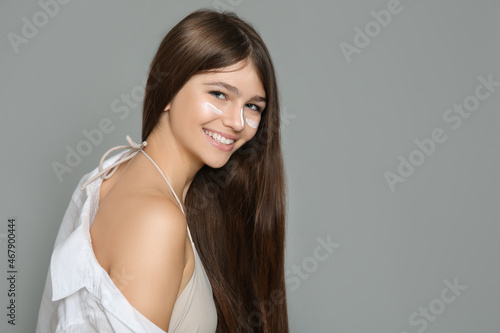 Teenage girl with sun protection cream on her face against grey background. Space for text