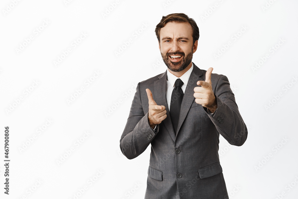 Enthusiastic corporate man, bearded guy in suit pointing fingers at camera, thumbs up, approve something, like and praise, standing over white background Enthusiastic corporate man, bearded guy in suit pointing fingers at camera, thumbs up, approve something, like and praise, standing over white background