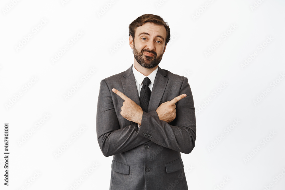 Indecisive corporate man in suit pointing sideways, two variants, making choice, looking confused, standing against white background Indecisive corporate man in suit pointing sideways, two variants, making choice, looking confused, standing against white background
