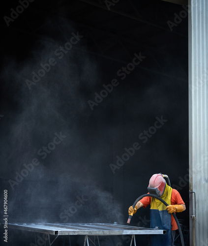 Male operator of sandblasting machine wearing protective uniform while polishing metal at workshop. Man preparing details for painting. 