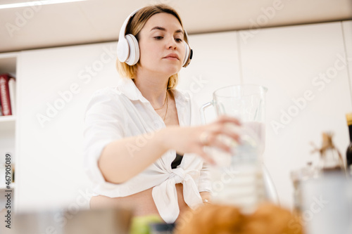 White pregnant woman in headphones making smoothy at home
