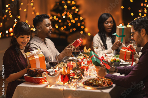 holidays  party and celebration concept - multiethnic group of happy friends having christmas dinner and giving presents at home